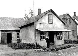 Vintage postcard - postally used in 1909 - shows the U.S. Custom House on Main Street in Franklin, Vt., with the U.S. Customs Service flag displayed and Customs Deputy Collector and Inspector Adolphus Dewing Whitney standing by the entrance.